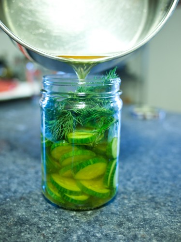 Pouring liquid over cucumbers and dill